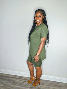 Woman wearing a dark olive 2 piece set standing against a white wall.