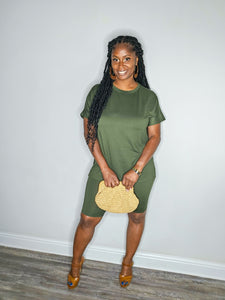 Woman wearing a dark olive 2 piece set standing against a white wall with a straw purse.